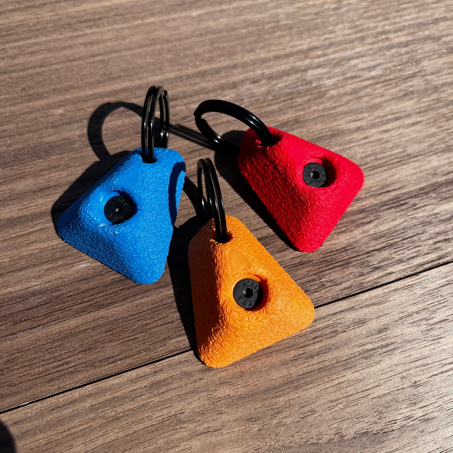 Three colorful keychains shaped like small rocks on a wooden surface