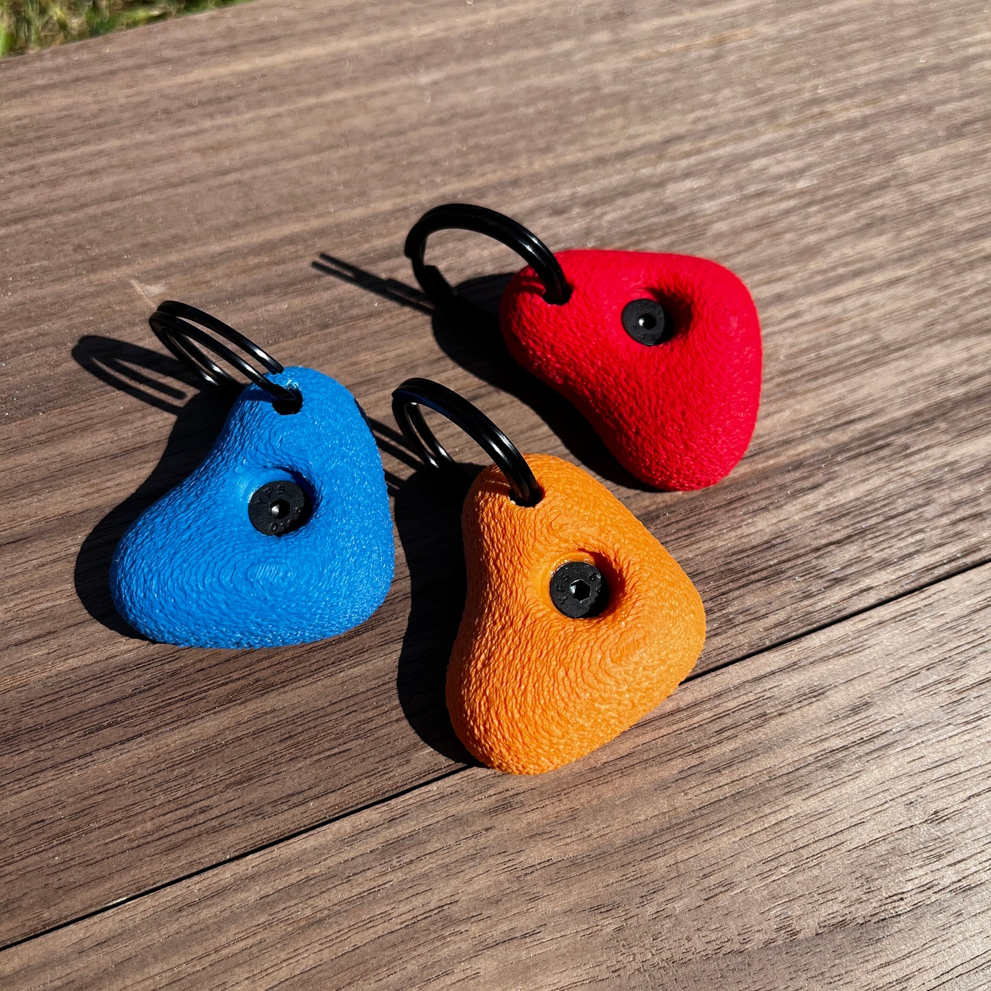 Three colorful rock climbing keyrings on a wooden surface
