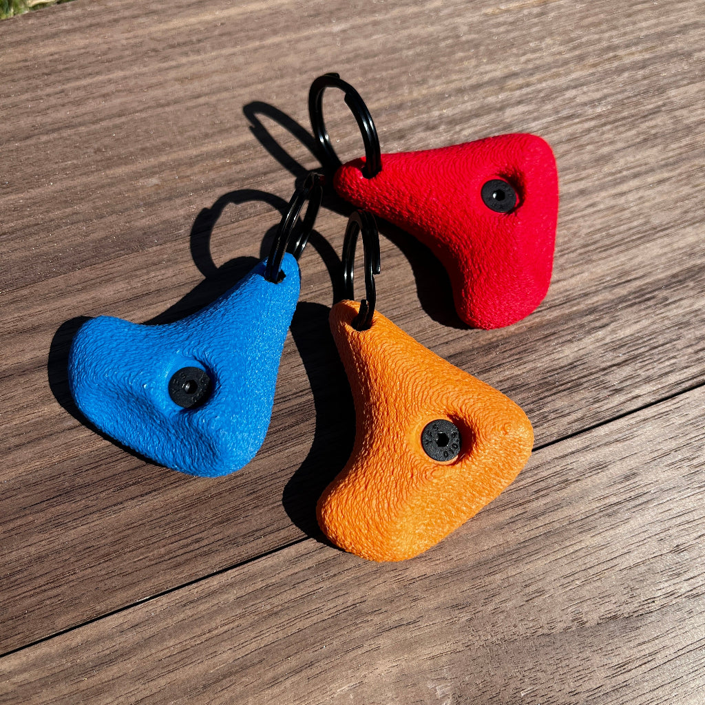 Three colorful keychains (red, blue, orange) on a wooden surface