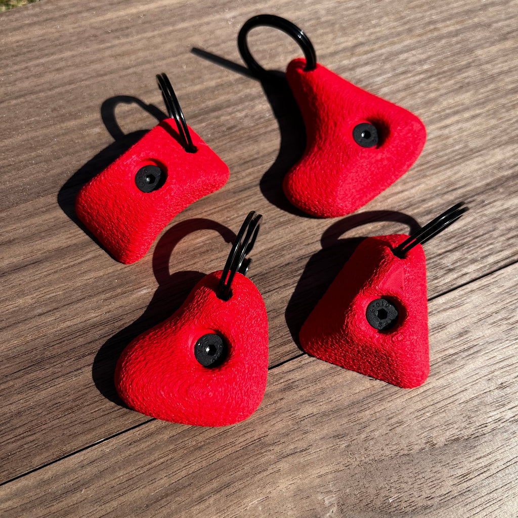 Four red keychains with black loops on a wooden surface