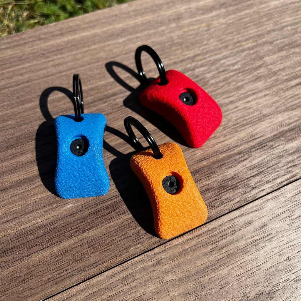 Three colorful keychains (blue, red, orange) on a wooden surface.