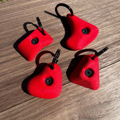 Four red keychains with black loops on a wooden surface