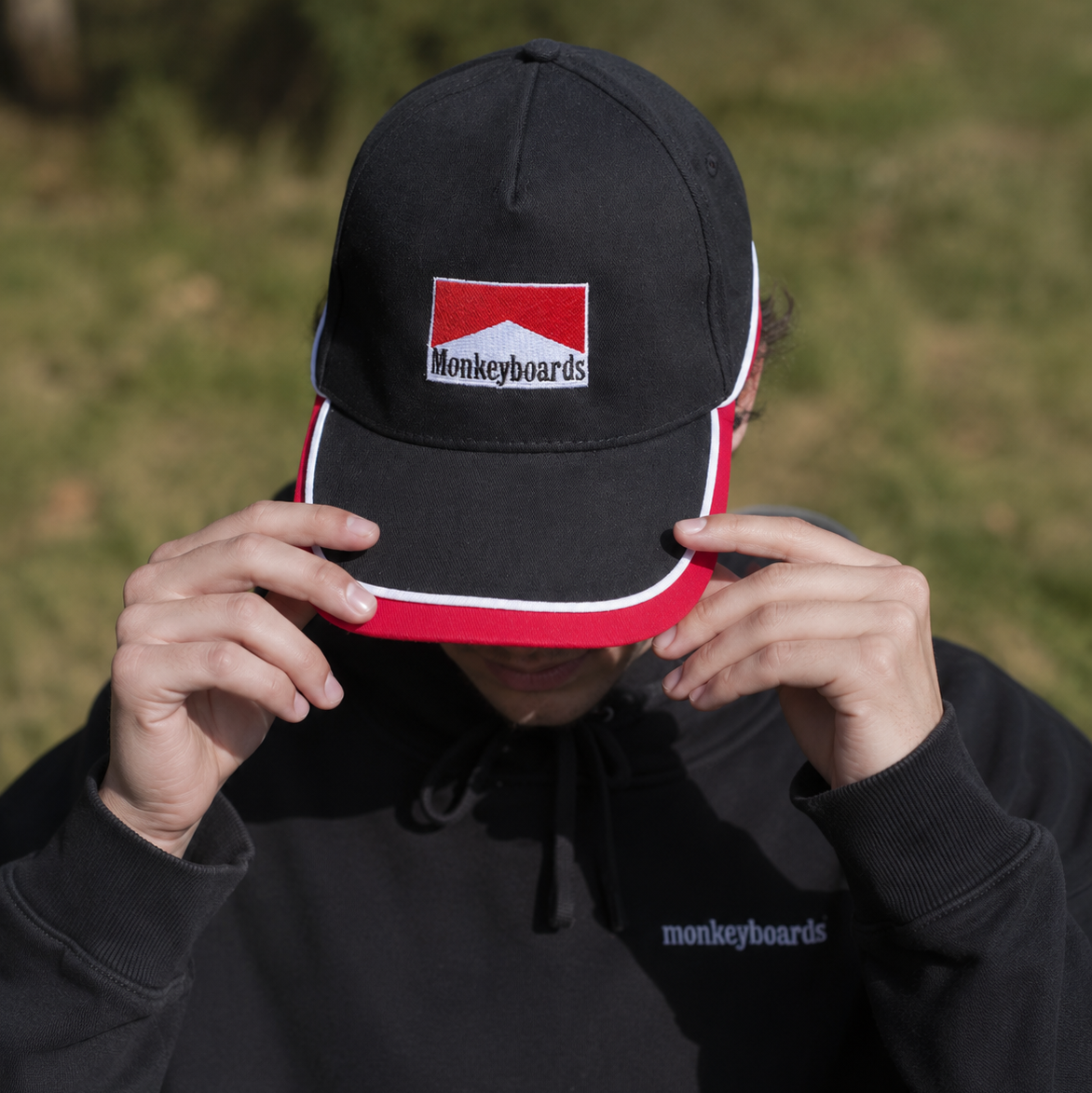 Person wearing a black cap with a red and white logo and matching black hoodie outdoors.
