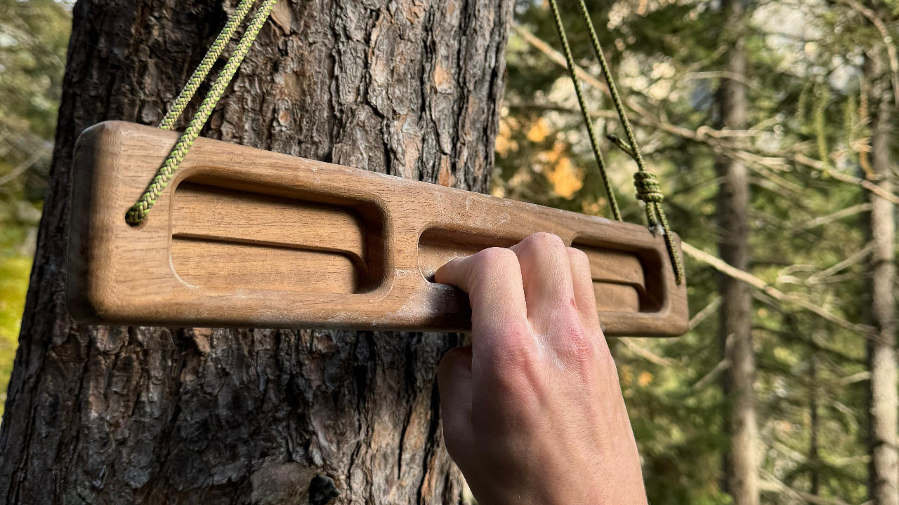 A walnut fullsize portable hangboard being used with one hand. Hanging on a tree in magic woods, switzerland.